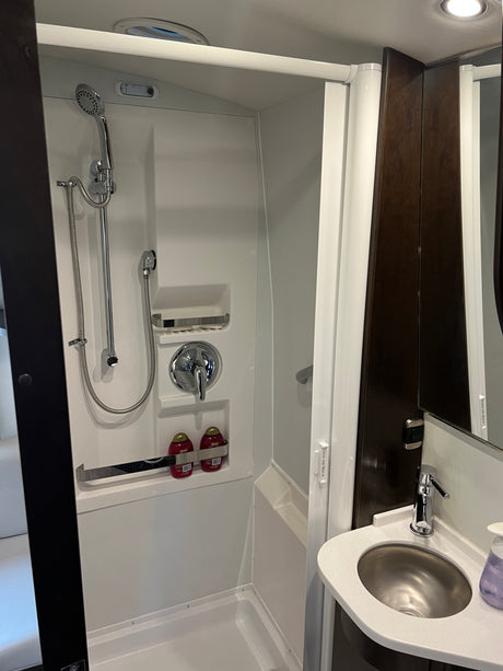Clean, compact bathroom in an RV rental, showcasing a white shower unit with a handheld sprayer and a small sink.