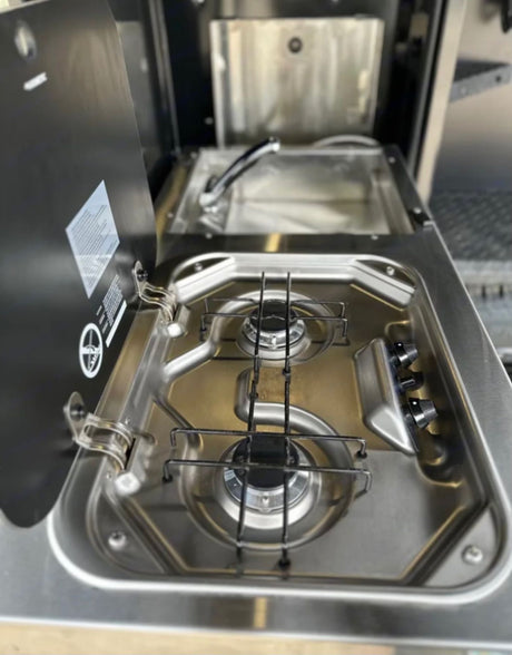 This compact stainless steel kitchenette, featuring a two-burner stove and sink, is perfect for an RV rental adventure.