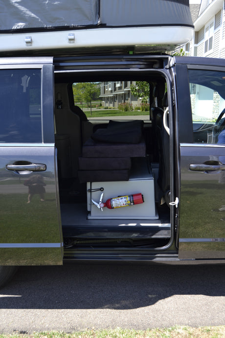 Camper van for RV rental: Minivan with open side door showing pop-top, interior cushions, and fire extinguisher.