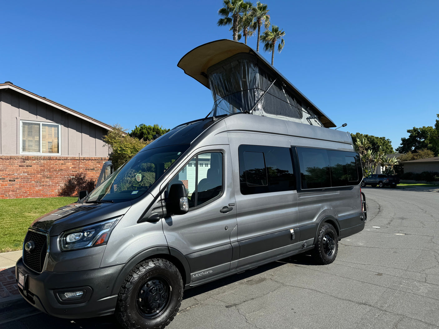 Gray ModVans camper van with pop-top roof extended, parked on a sunny street. Perfect for an rv rental adventure!