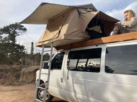 RV rental: Van with rooftop tent & ladder, plus a person enjoying the scenic outdoor campsite. Perfect for van life adventures!