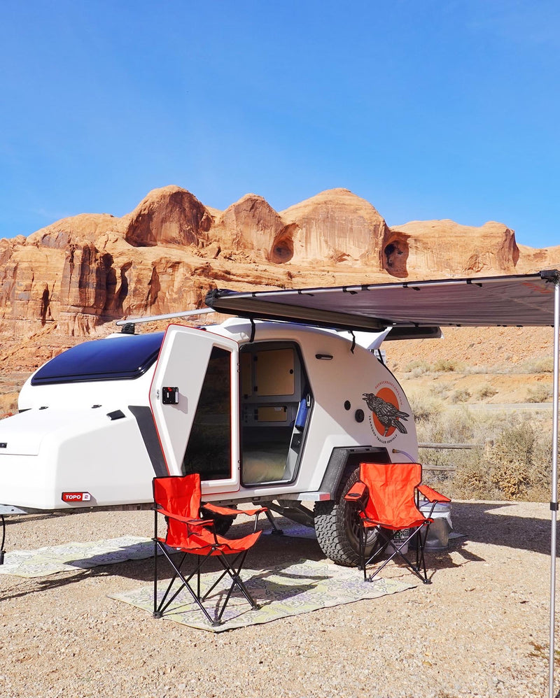 This white teardrop RV rental is set up for desert camping, with chairs and awning, backed by majestic red rock formations. — photo 15
