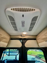 Inside an RV rental: The modern ceiling AC unit with climate control, overhead storage, and outdoor views from the windows.