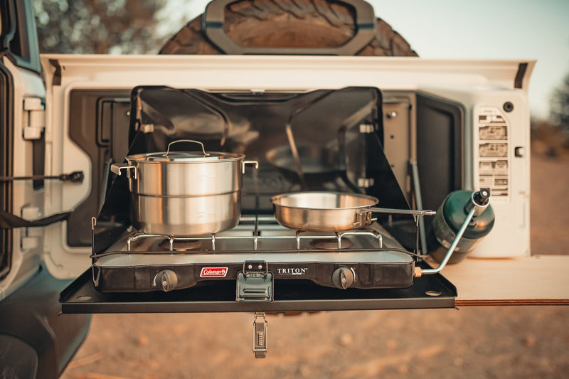 RV rental adventure: A Coleman Triton stove, pot & pan on a pull-out kitchen from an off-road vehicle, ready for camping. — photo 3