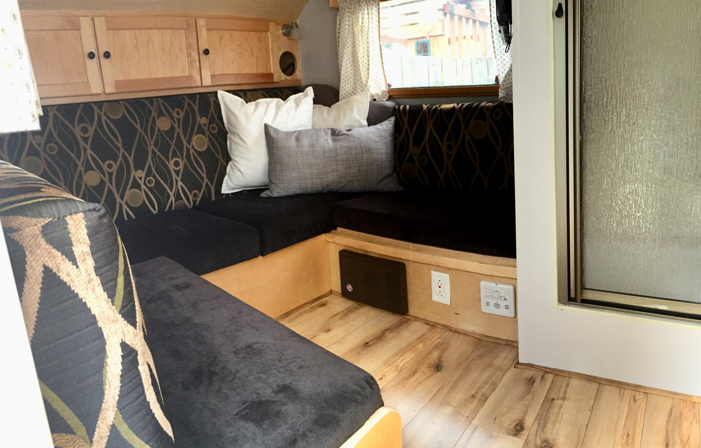 Cozy RV rental interior with a dinette featuring patterned cushions, wood cabinets, and light flooring. Includes outlet & detector.