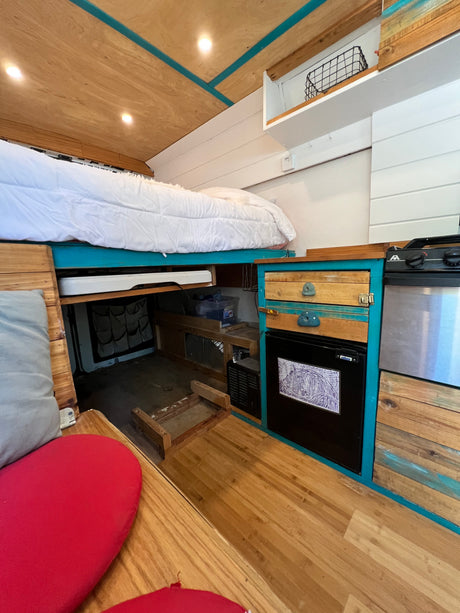 Cozy RV rental interior with elevated bed, compact kitchen, and wooden accents.