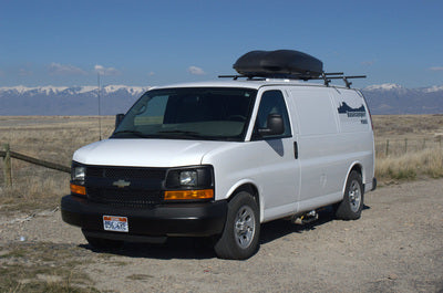 White cargo van with roof rack, ideal for RV rental adventures, parked on a dirt road with snow-capped mountains in the distance.