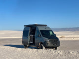 This gray Mercedes-Benz RV rental, a camper van with off-road tires, is parked on white gypsum dunes under a clear blue sky.