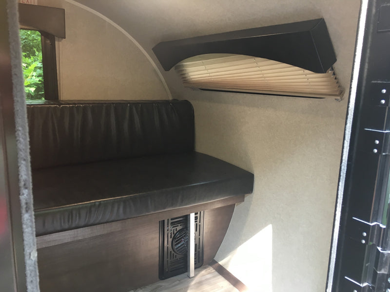 Interior of an RV rental showing a dark upholstered bench seat, side window, and pleated blinds over another window. A floor vent is visible. — photo 7