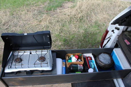 RV rental outdoor kitchen setup: a pull-out drawer from a vehicle with a camping stove, utensils, & supplies.