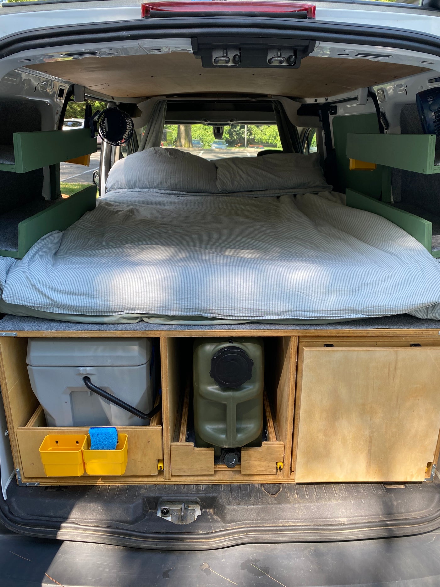 RV rental: Camper van interior with cozy bed, built-in storage for a portable toilet & water, fan, and side shelves. — photo 4