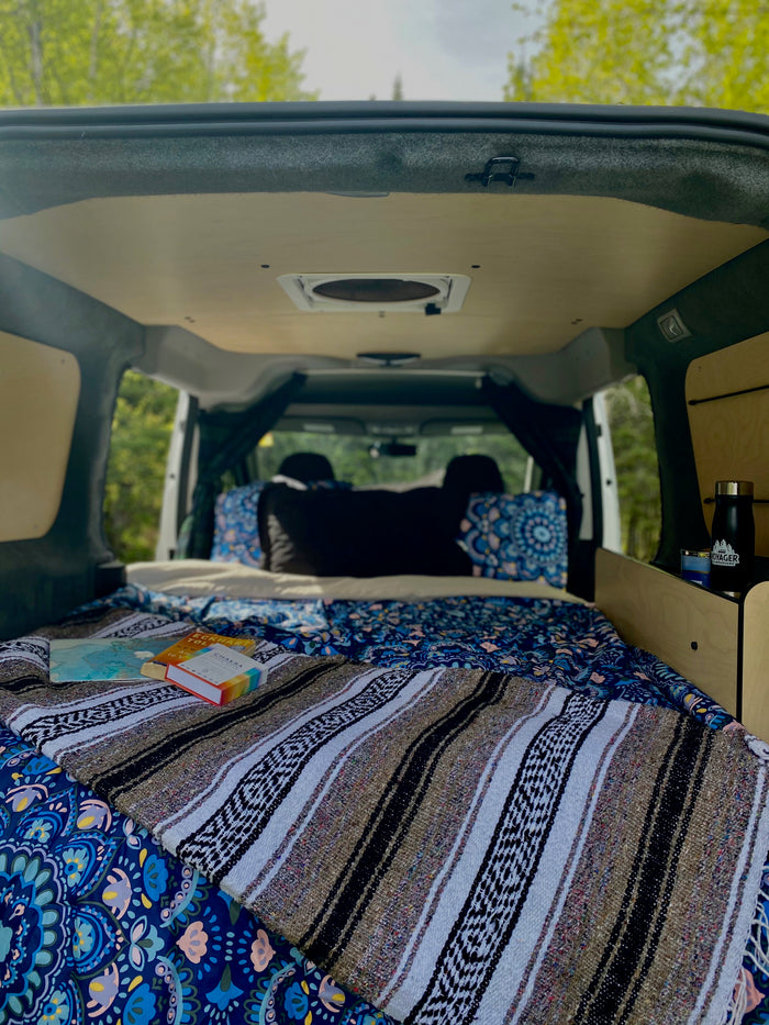 Cozy camper van interior: a perfect RV rental setup for relaxing road trips, complete with a bed, books, and nature views.