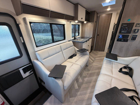 This RV rental interior showcases light leather sofas, a compact kitchen, and modern controls on light wood floors.