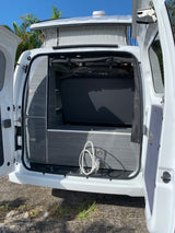 RV rental: Rear interior of a white pop-top camper van with doors open, showing a bed, grey storage, and outdoor shower hookup.