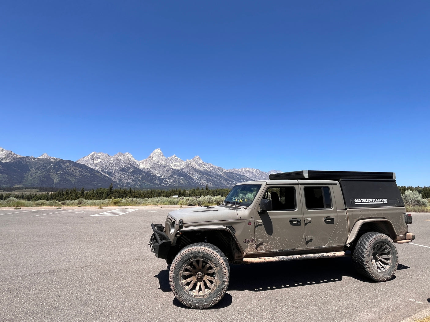 Gray Jeep Gladiator with rooftop tent in a mountain parking lot, ready for adventure. Ideal for an RV rental or overland trip.