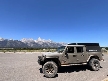 Gray Jeep Gladiator with rooftop tent in a mountain parking lot, ready for adventure. Ideal for an RV rental or overland trip.