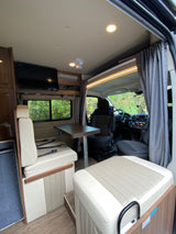 Inside a modern RV rental: dining table, comfy seats, TV, and driver's cabin view for your road trip comfort.