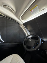 Interior of an RV rental van, featuring custom black window insulation panels, steering wheel, and light-colored seat.