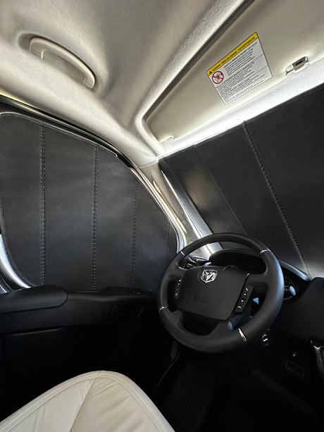 Interior of an RV rental van, featuring custom black window insulation panels, steering wheel, and light-colored seat.