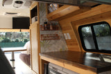 Stylish RV rental interior: wood-paneled kitchen with Dometic cooler, cozy dining area, and TV. Ideal for travels.