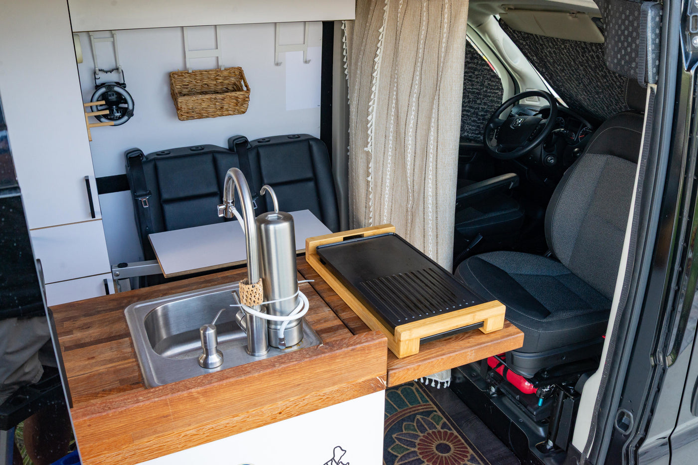 This RV rental's van interior features a practical kitchen area with a sink, water filter, and griddle, plus passenger seating. — photo 6