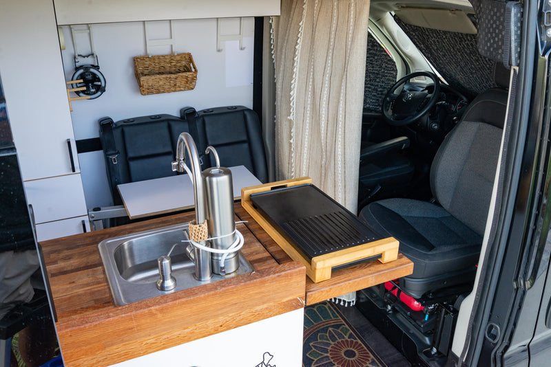 This RV rental's van interior features a practical kitchen area with a sink, water filter, and griddle, plus passenger seating. — photo 6