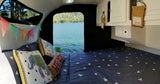 Inside a comfortable RV rental: a cozy bed, colorful bunting, and a serene lake view from the large opening.