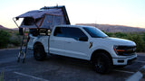 Light grey Ford F-150 pickup with a Roofnest rooftop tent, perfect for an rv rental overlanding trip in a scenic desert.