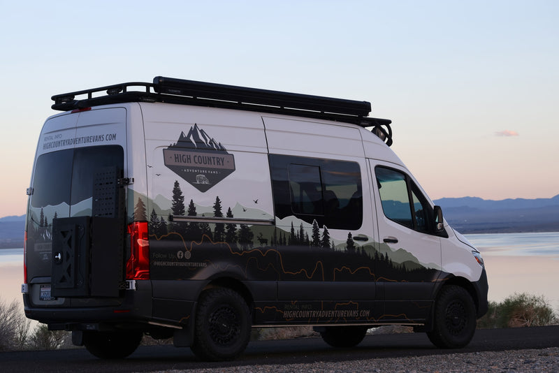 Custom-wrapped adventure rv rental van, with mountain graphics and roof rack, parked by a serene lake at dusk. — photo 1