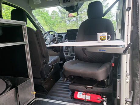 This RV rental's front cabin interior features a practical Lagun table, swiveled passenger seat, and fire extinguisher, perfect for van life.