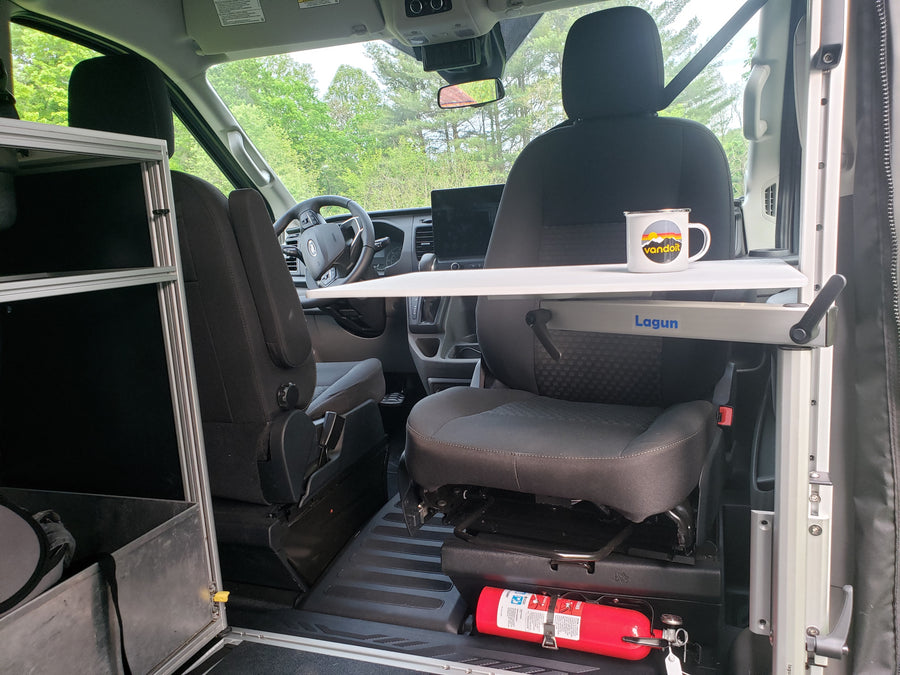 This RV rental's front cabin interior features a practical Lagun table, swiveled passenger seat, and fire extinguisher, perfect for van life.