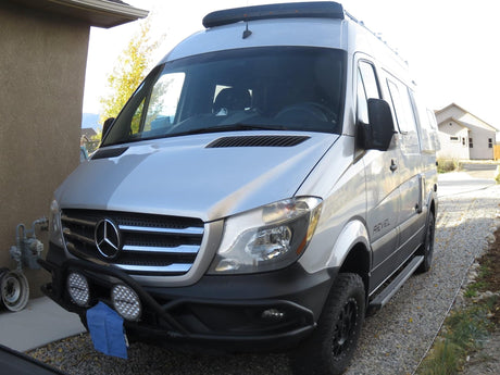 Silver Mercedes-Benz Sprinter van, equipped for adventure, parked on a gravel driveway. Perfect for your next rv rental.