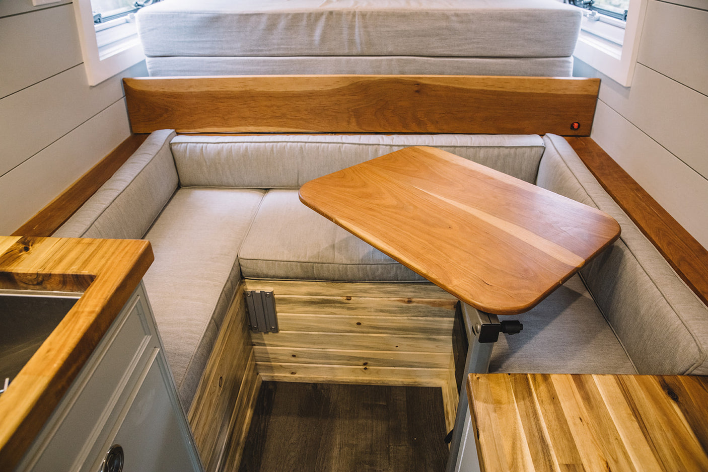 Cozy RV rental interior featuring a wooden dinette table, L-shaped seating with light grey cushions, and a small kitchen counter.