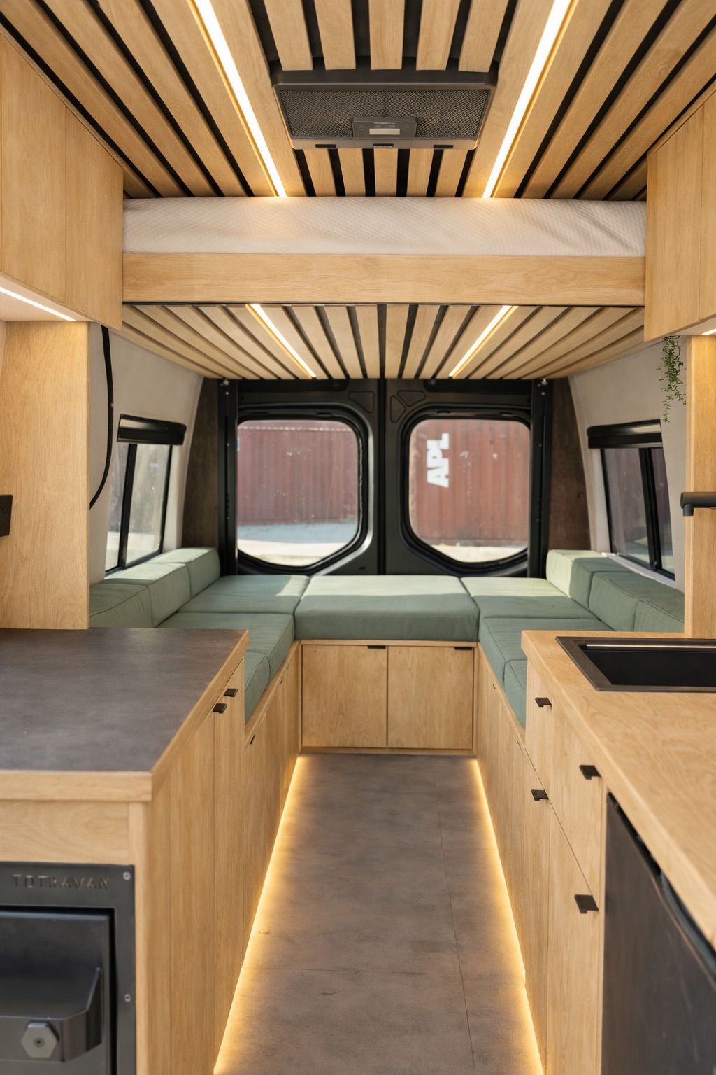 Modern RV rental interior with wood details, U-shaped seating, kitchen, and bed, ideal for van life adventures.