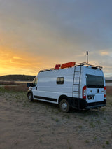 This white RV rental van, equipped for adventure, sits by a serene lake under a vibrant sunset, perfect for a Texas road trip.