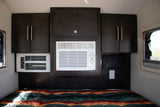 Inside a cozy rv rental: bed, dark cabinets, and dual AC units ensure comfort for travelers.