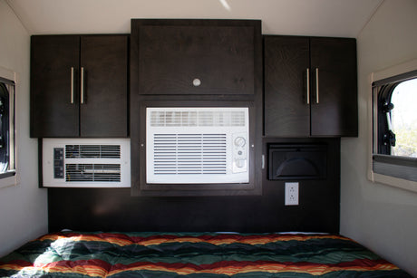 Inside a cozy rv rental: bed, dark cabinets, and dual AC units ensure comfort for travelers.