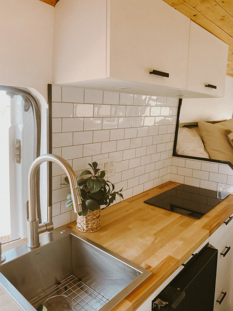 RV rental: Bright kitchen with a stainless steel sink, induction cooktop, wood counters, white subway tile, and overhead cabinets. — photo 4