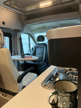 Inside an RV rental: compact kitchen with stove, comfortable swivel seating, and table for road trip adventures.