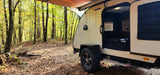Enjoy nature! This cozy teardrop RV rental, parked in a vibrant forest, welcomes you with an open door to a bed and AC.