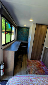 Spacious RV rental interior featuring a modern desk, cozy bed, large window with outdoor views, and a stylish accent wall.