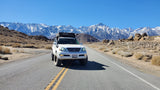 White Lexus GX with rooftop tent on a desert road, snow-capped mountains. A unique choice for your RV rental adventure.