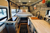 Explore this stylish RV rental interior! Features a cozy bed, full kitchen with sink & stove, wood walls, and thoughtful storage.