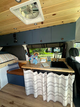 Cozy rv rental interior: wood ceiling, bed, kitchen with sink & storage. Perfect for travel adventures.