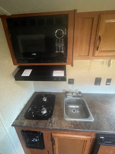 RV rental kitchen: Features a built-in microwave, two-burner stove, and sink on a countertop with wooden cabinets.