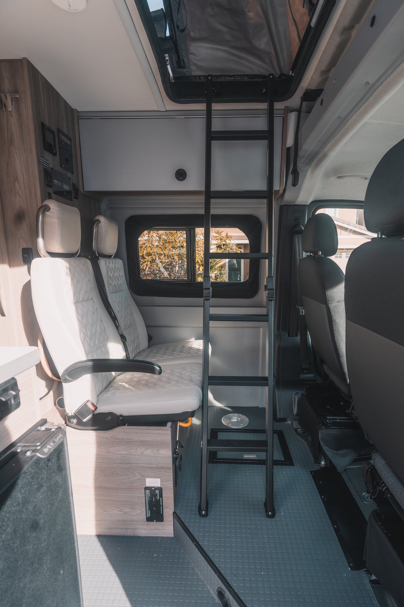 Inside this rv rental: light seating, a ladder to the pop-top sleeping area, wood panels, and textured gray flooring.