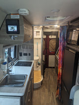 This rv rental features a compact kitchen with a sink & cooktop, a bathroom, and a control panel for comfortable on-the-go living.