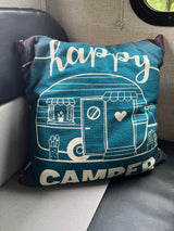 "Happy Camper" pillow in an RV rental. Teal fabric with white camper graphic, adding a cozy touch to the interior.