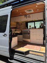 Explore this modern RV rental's cozy interior, featuring a full kitchen, bed, and seating area. Ideal for van life adventures.