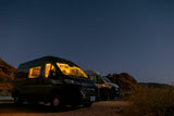 Cozy rv rental vans illuminate a dark, star-lit desert night, parked against rugged rock formations.